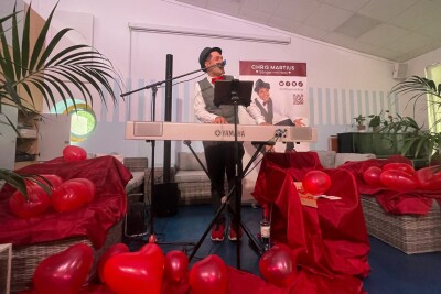 Chris Martius spielt Klavier und singt und ist umringt von vielen roten Herz-Luftballons