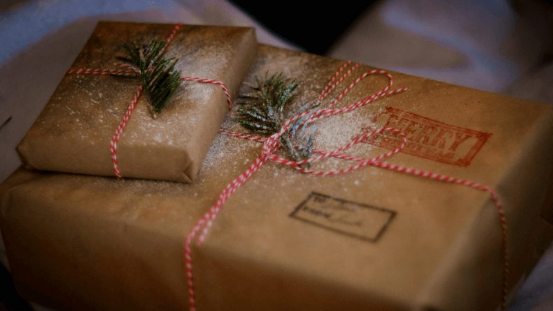 Zwei festlich verpackte Geschenke, übereinander gestapelt und dekoriert mit Tannenzweigen und künstlichem Schnee