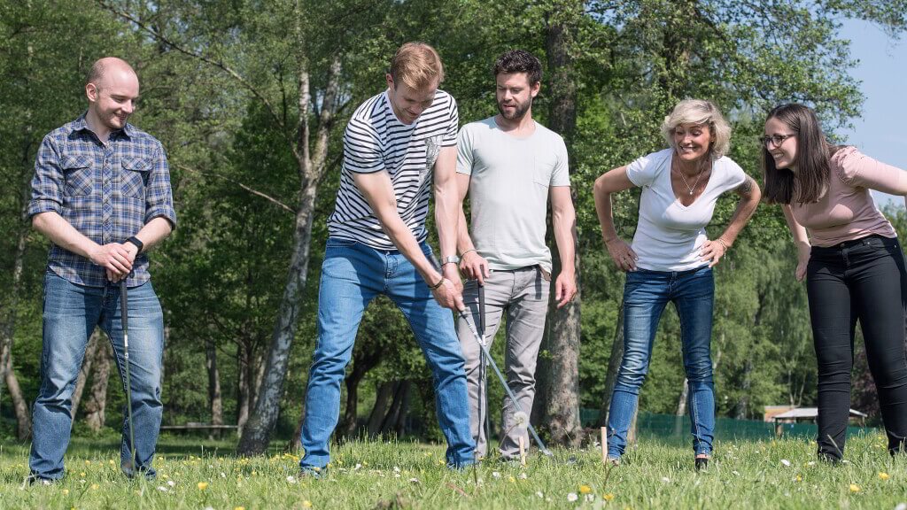 Fünf Personen stehen auf einer Wiese, ein Mann hat einen Mini-Golf Schläger in der Hand.