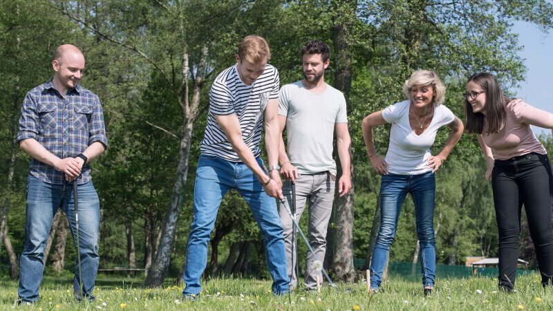Fünf Personen stehen auf einer Wiese, ein Mann hat einen Mini-Golf Schläger in der Hand.