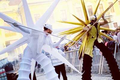 2 Stelzenläufer in weiß und gold inmitten eines Festivals